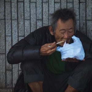 pexels-photo-1657936-1657936 Elderly man sitting and eating on a Kowloon street, capturing urban life.